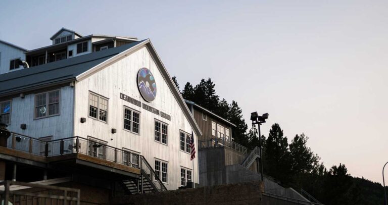 a building is shown in front of a hill with dark pine trees behind